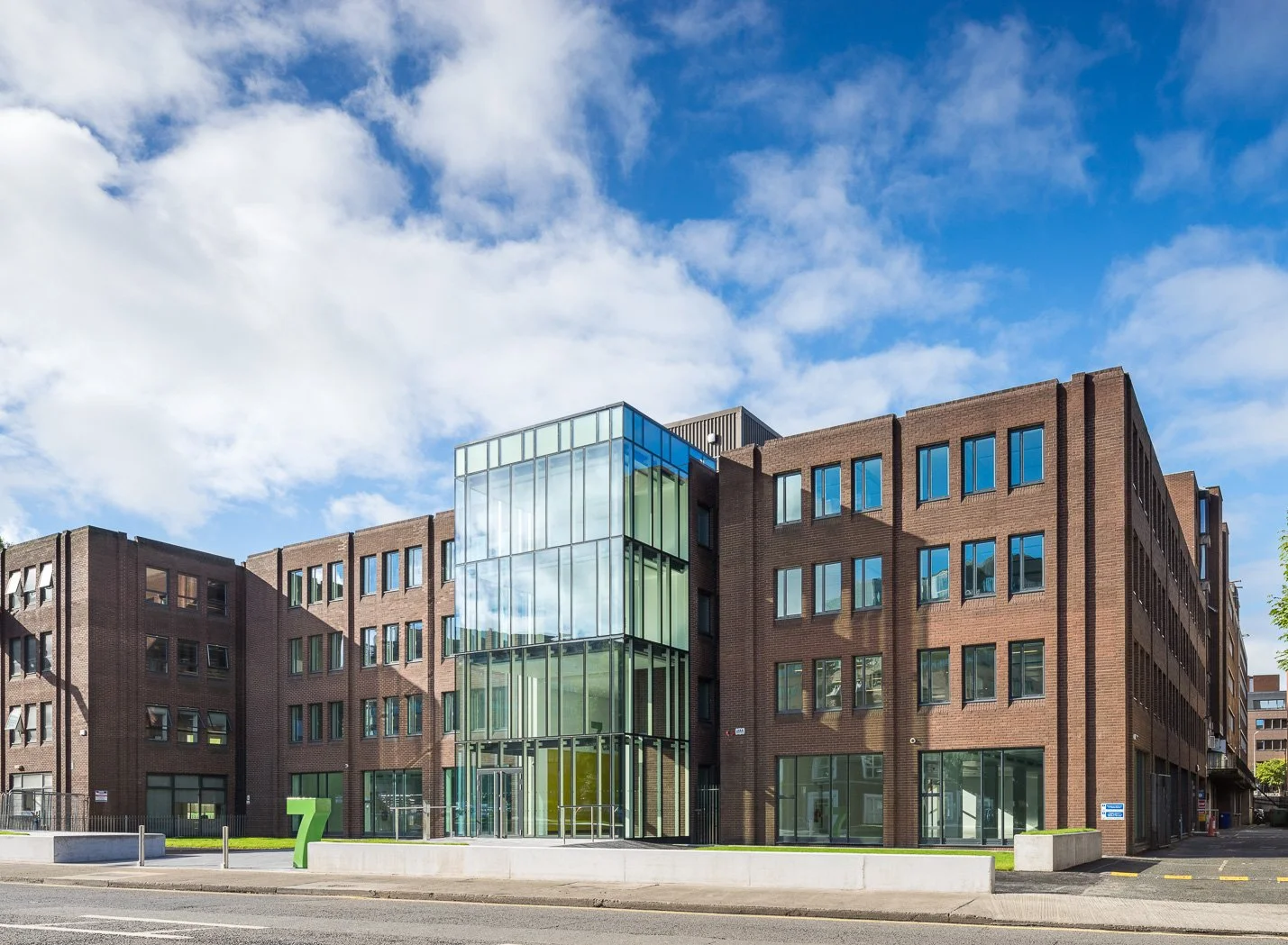 Modern brick building with glass entrance and blue sky with clouds.