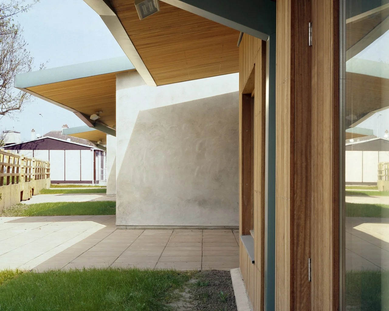 View of modern building exterior with wooden and concrete elements, large windows, and a backyard with grass and paved patio.