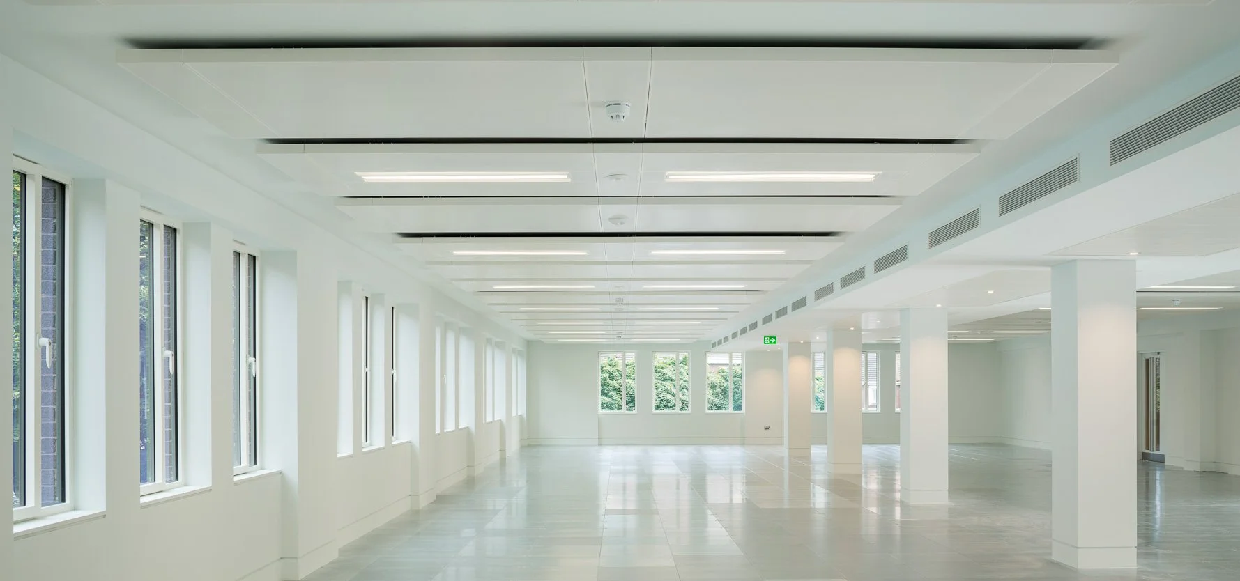 Empty modern office or conference room with large windows, white walls, light-colored floor, and ceiling lights.