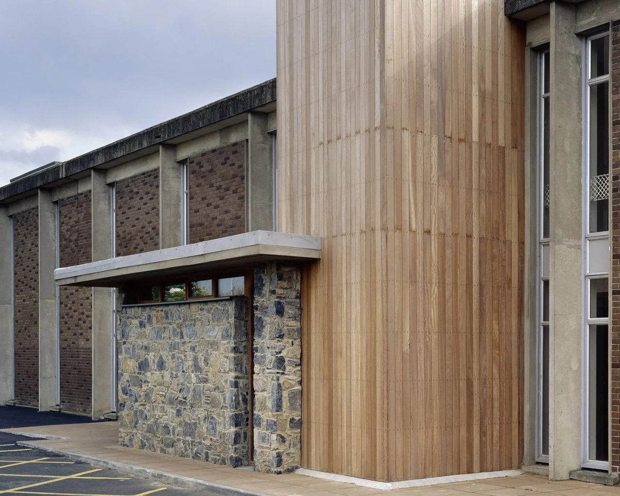 Close-up of a modern building featuring a stone wall, wooden paneling, and brick and concrete architectural elements.