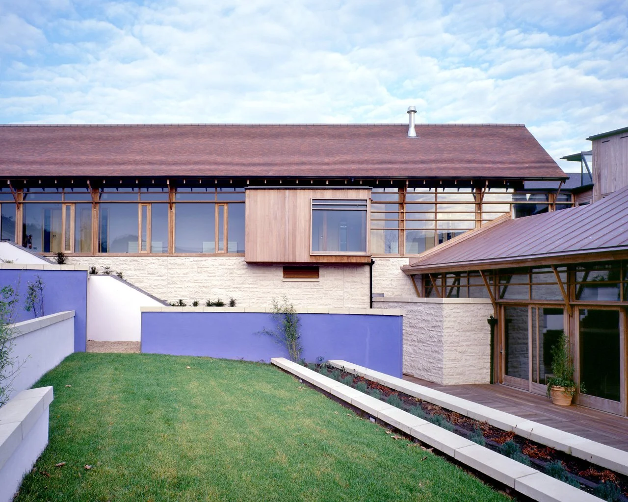 Modern house with large windows, wooden accents, and a landscaped green lawn with a pathway.