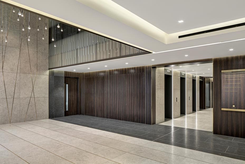 Modern lobby with elevators, dark wood paneling, stone walls, and recessed lighting.