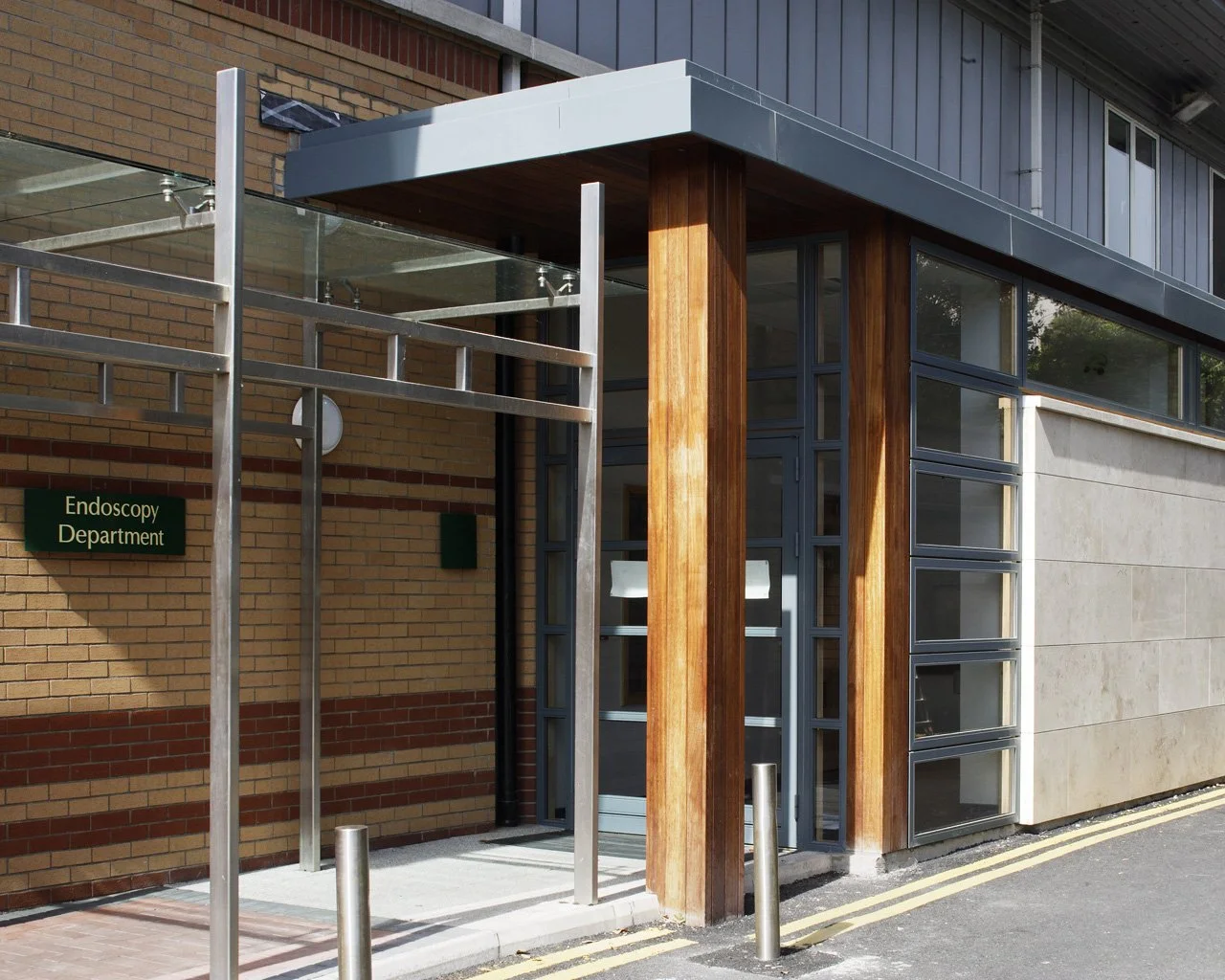 Exterior view of a modern building with a sign indicating it is the Endoscopy Department, featuring brick and concrete walls, large glass windows, and wooden and metal accents.