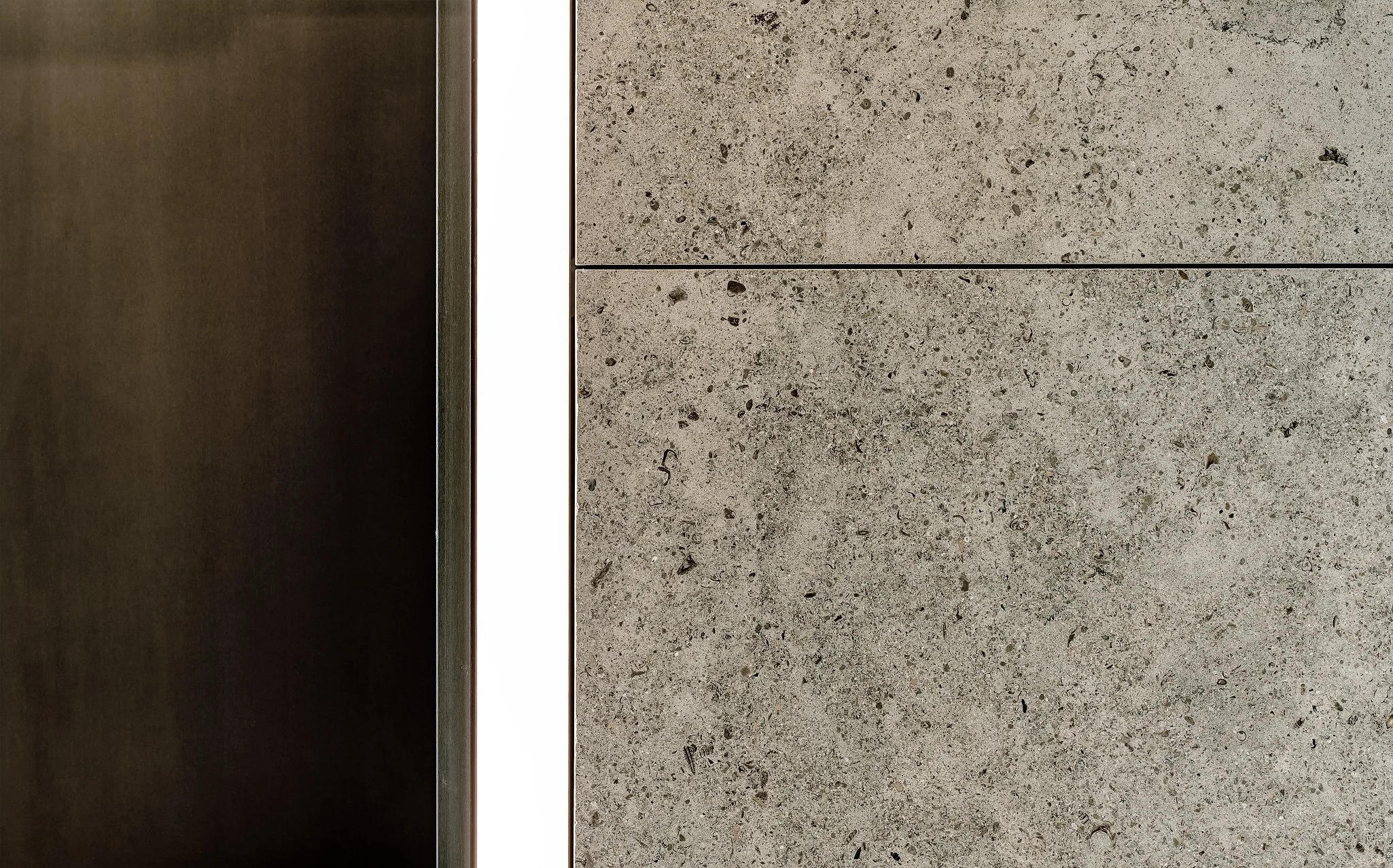 A close-up view of a textured, light gray concrete wall with black specks and mortar lines, with a vertical dark wood panel on the left side.