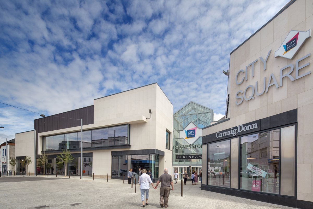 People walking towards the entrance of City Square shopping mall, with store signs including Craig Dann and Dunestow, under a partly cloudy sky.
