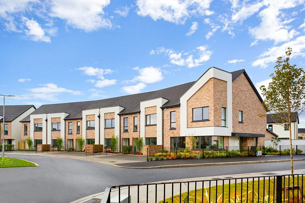 Modern townhouses with brick facades and large windows under a blue sky with clouds.