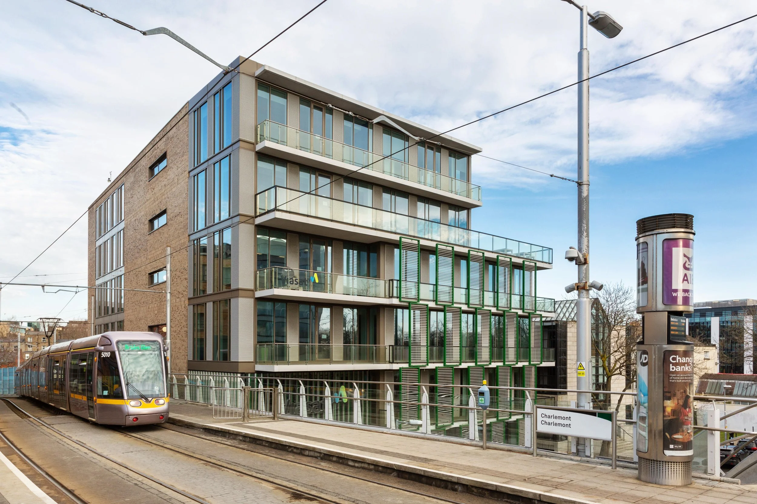 Modern multi-story building with glass balconies and green window shutters, tram tracks in front, a tram on the left side, and a Charenton Charlemont sign at a tram station.