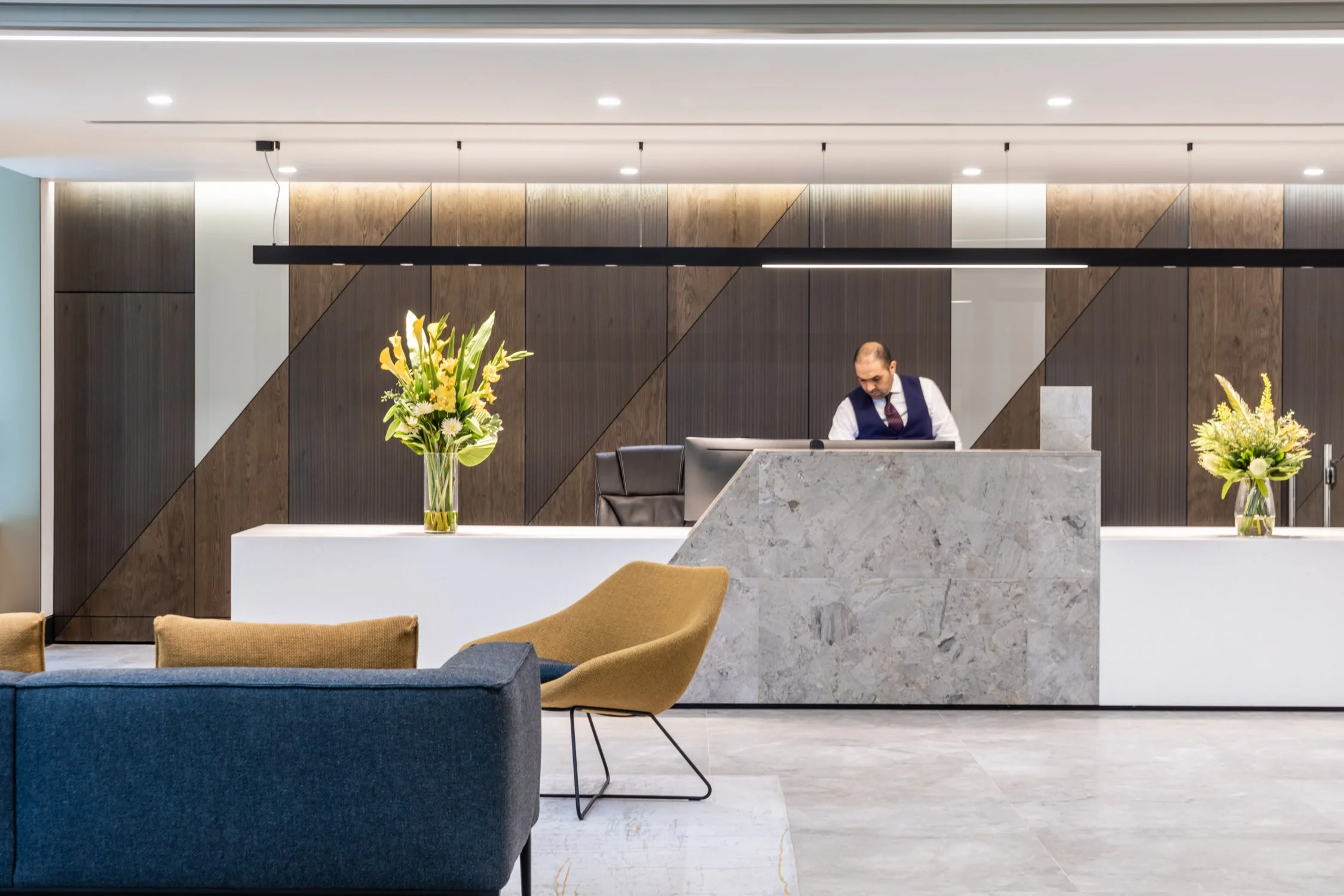 Modern hotel reception area with a front desk, floral arrangements, and seating.
