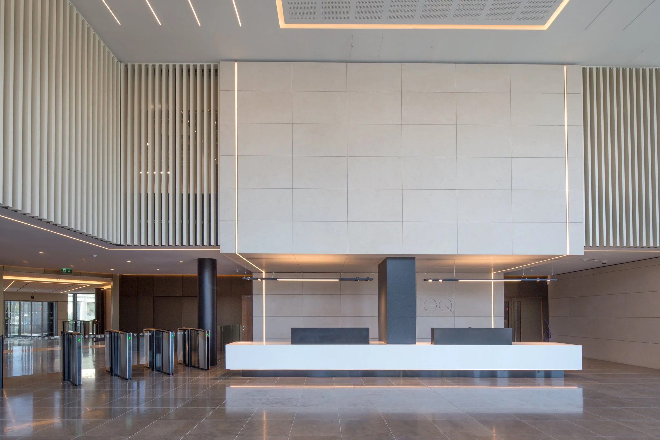 Modern building lobby with a sleek white reception desk, black support columns, and a decorative wall with vertical slats and lighting accents.
