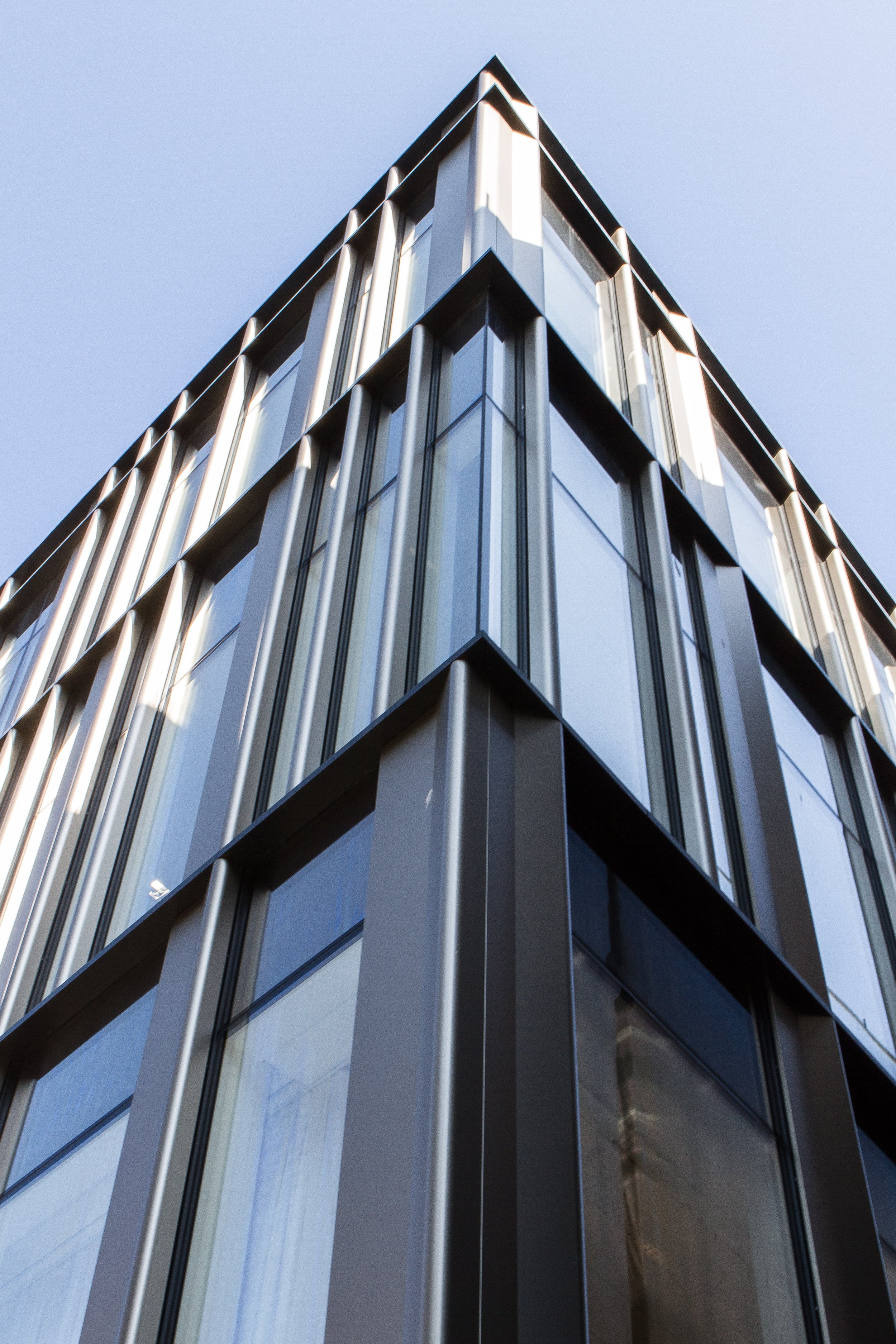 Modern glass and metal building viewed from below, with a clear blue sky in the background.