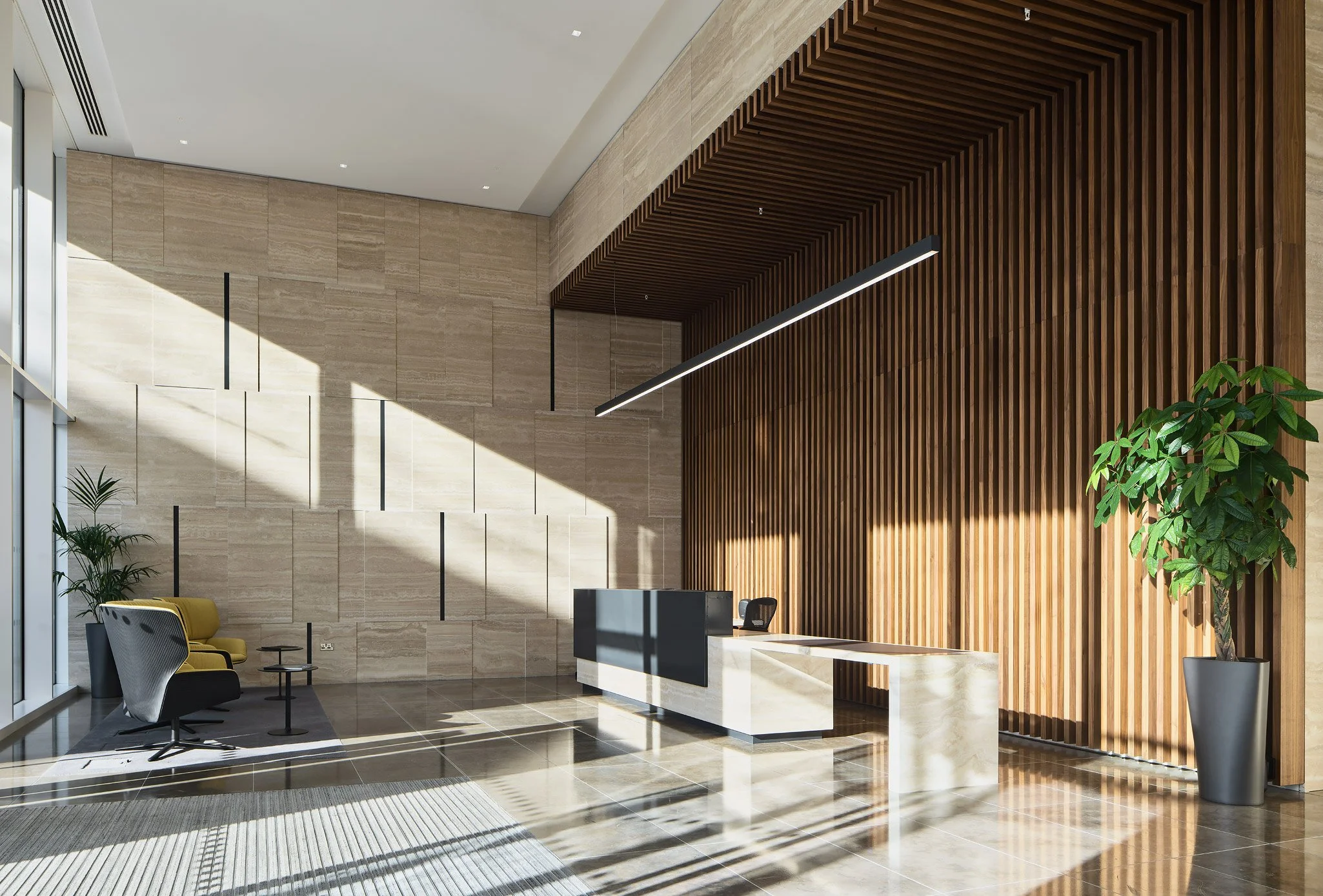 Modern office lobby with a reception desk, two black and yellow chairs, potted plants, wooden panel wall, and large windows allowing sunlight.
