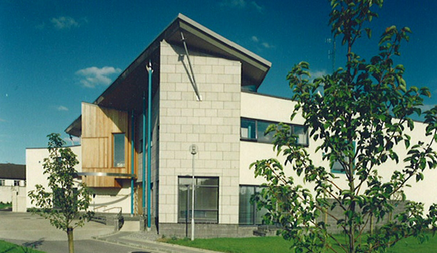 Modern school building with large windows, trees, and a blue sky.