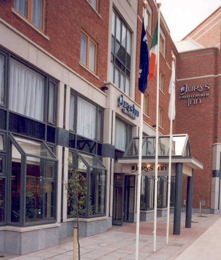 Exterior of the Jurys Inn hotel in Christchurch, showing the entrance, windows, chairs, and flags including Ireland's flag.
