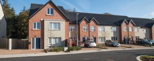 A row of modern townhouses with parked cars in front and a clear blue sky.