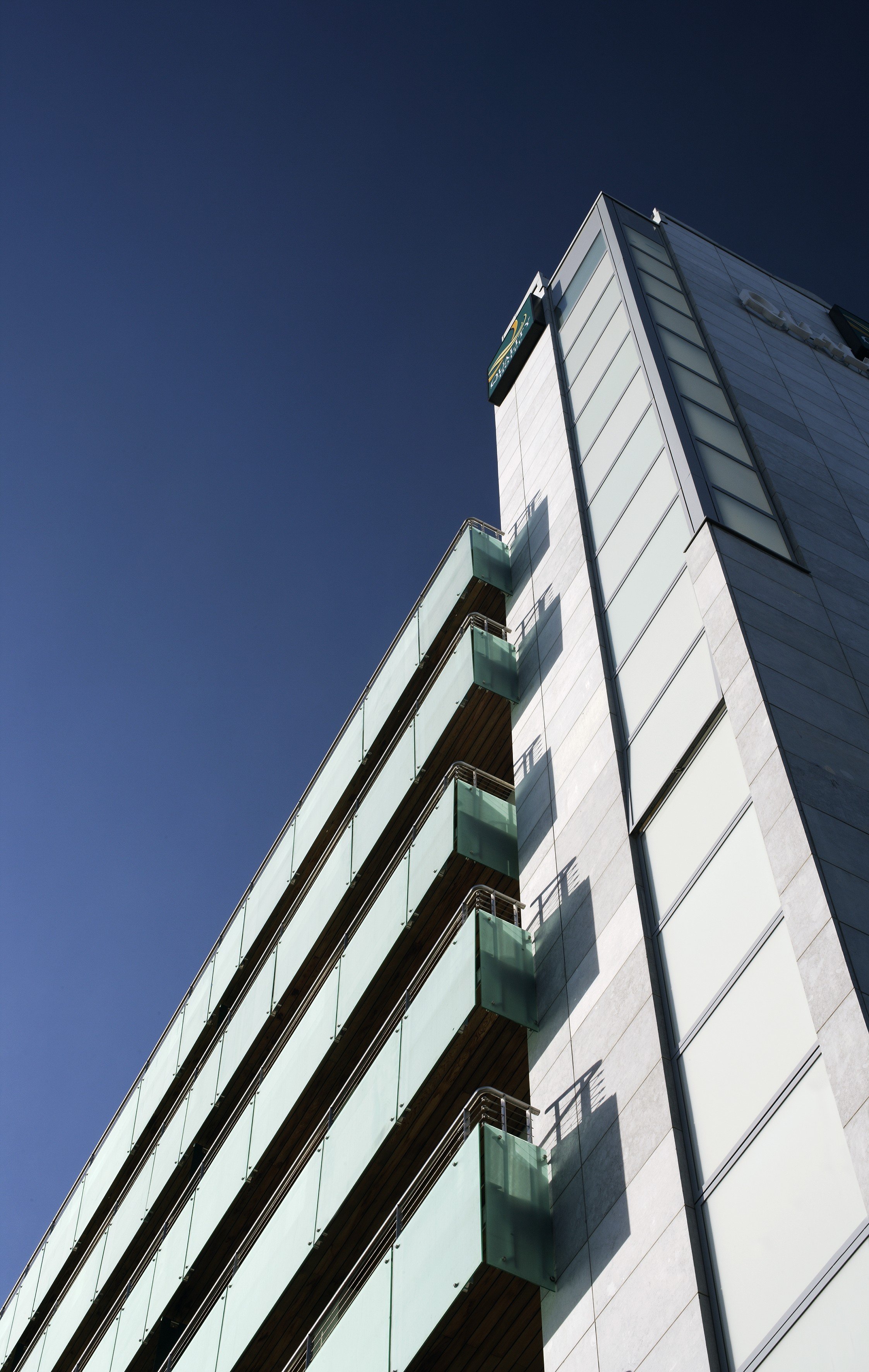 Low-angle view of a modern building with glass balconies and a clear blue sky.