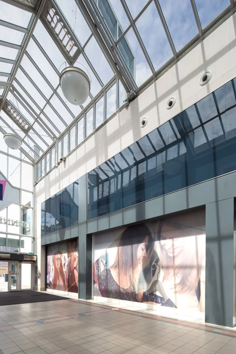 Inside a modern shopping mall with a glass roof and large advertisements on the walls showing women shopping and talking.