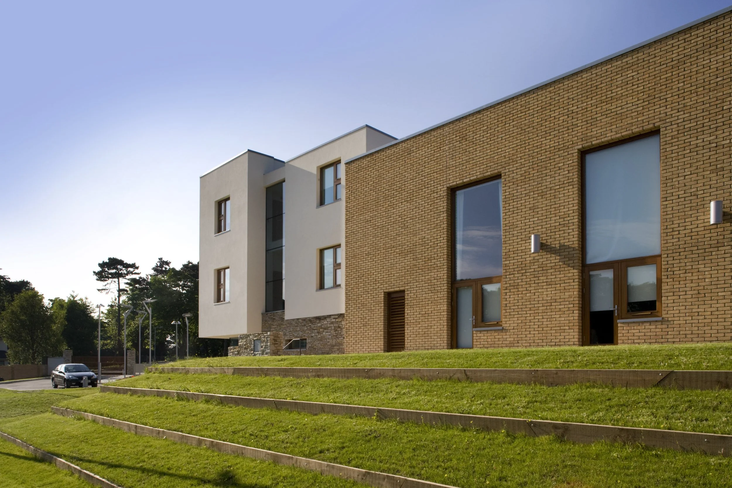 Modern multi-story residential building with white and brick exterior, large windows, and a landscaped lawn in the foreground.