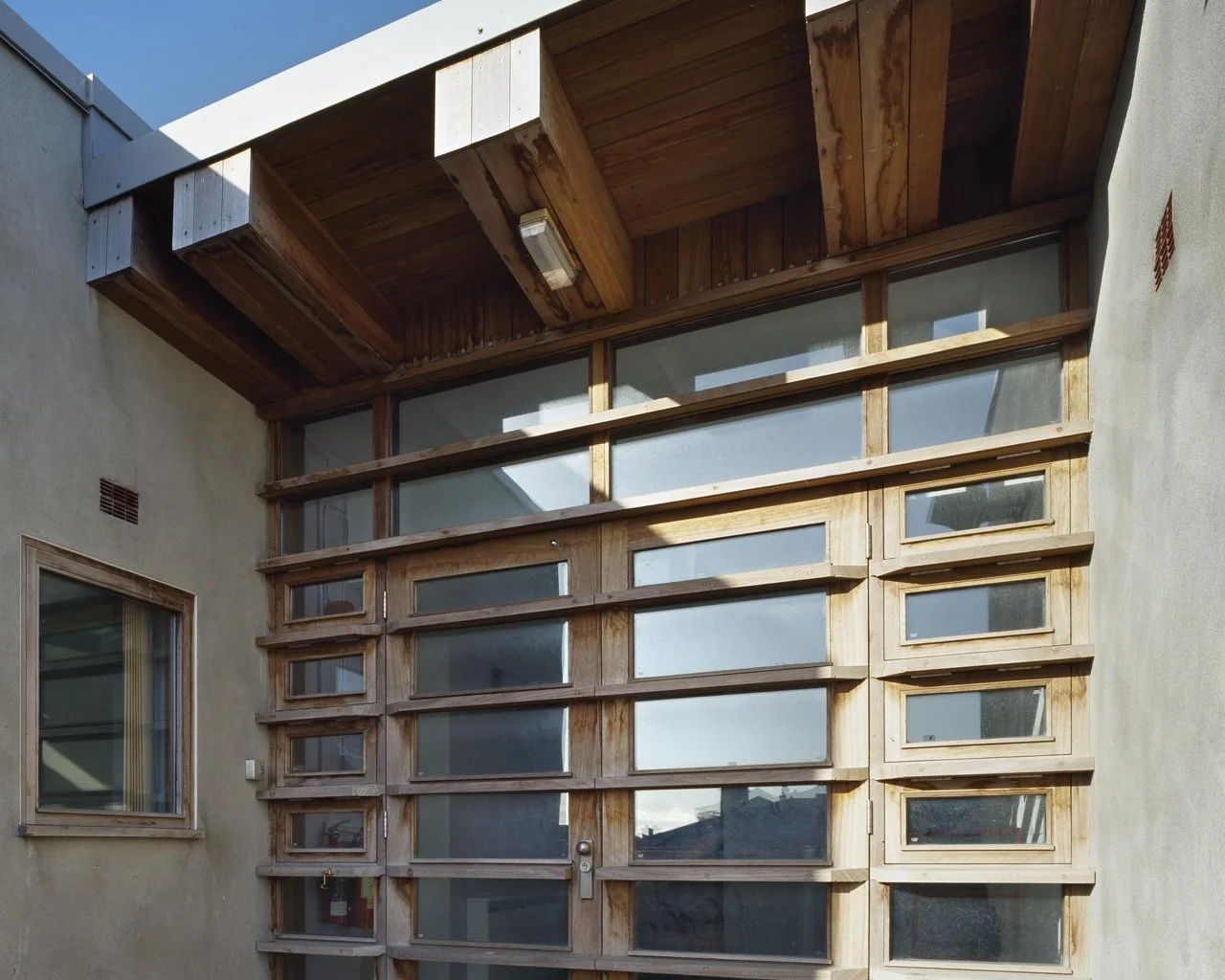 Exterior view of a modern building featuring a large glass door and a window, with a wooden overhang and decorative wooden framework.