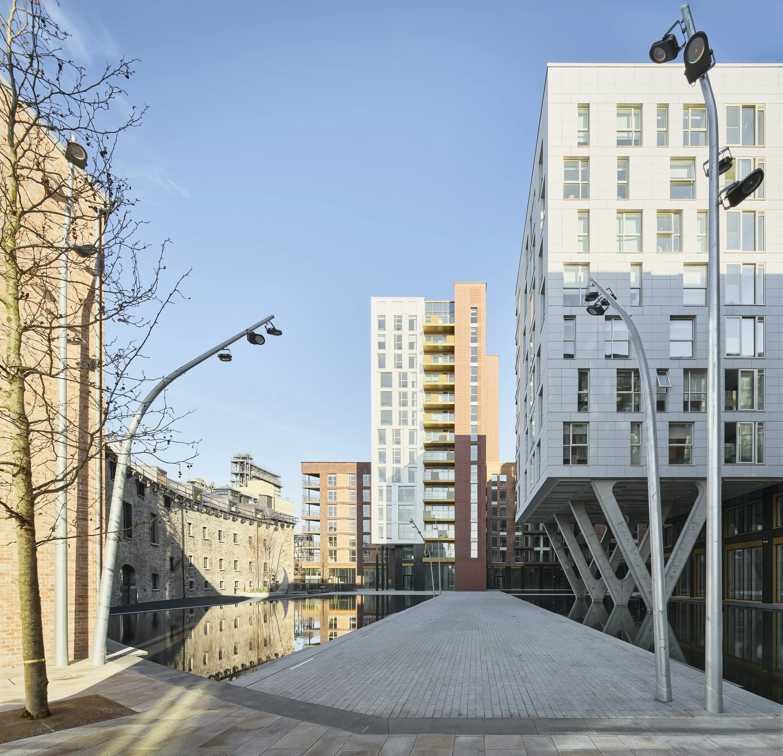 Modern buildings, street lamps, and a small body of water in an urban area with clear blue sky.