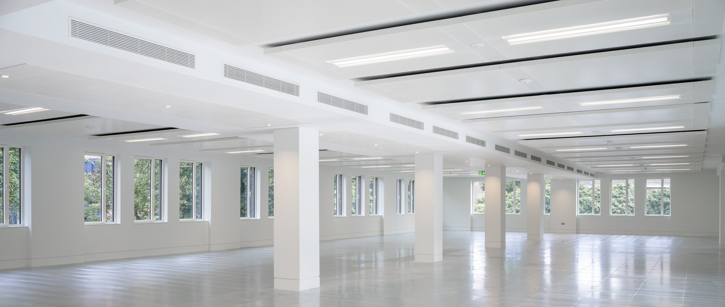 Empty interior space with white walls, large windows, and a white ceiling with modern lighting fixtures.