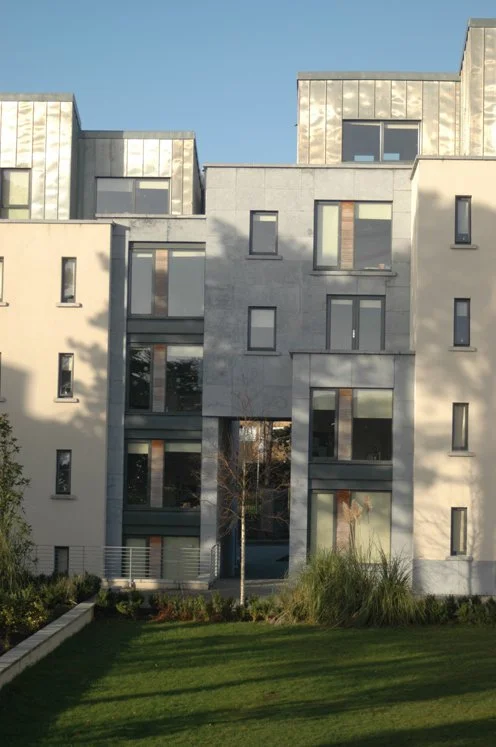 Modern multi-story apartment building with a landscaped lawn and trees in front.