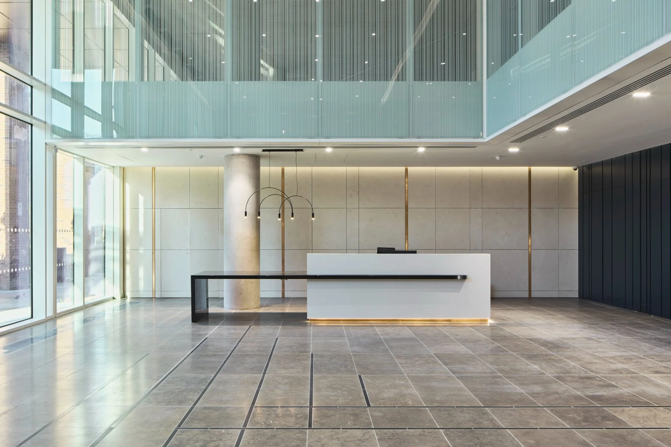 Modern hotel lobby reception area with a white desk, black accents, tiled flooring, large windows, and minimalist design.
