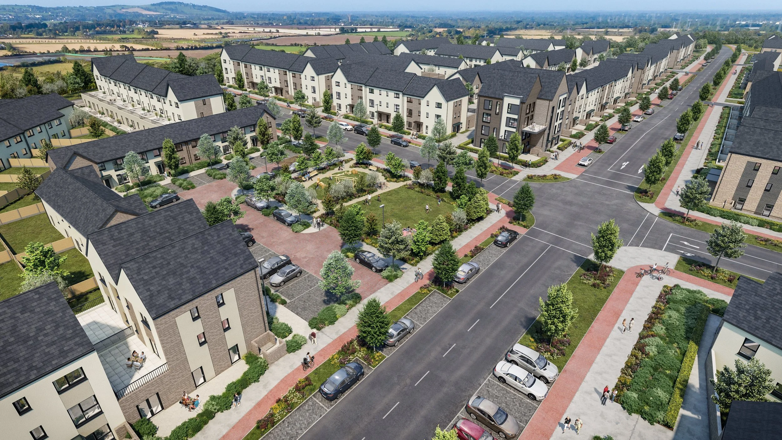 Aerial view of a modern residential neighborhood with townhouses, green spaces, trees, and parking areas, with a wide street and sidewalks.