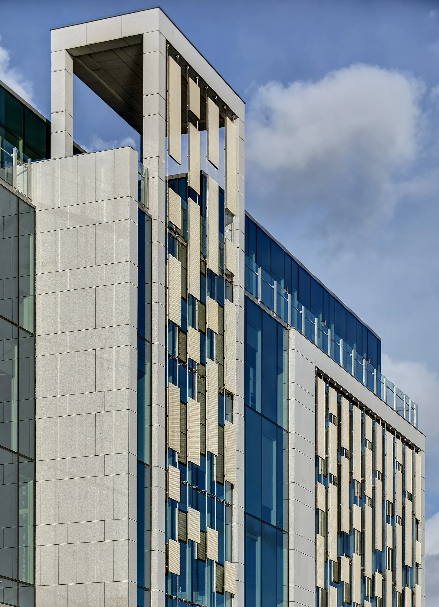 Modern building with glass windows and architectural details against a blue sky with clouds.