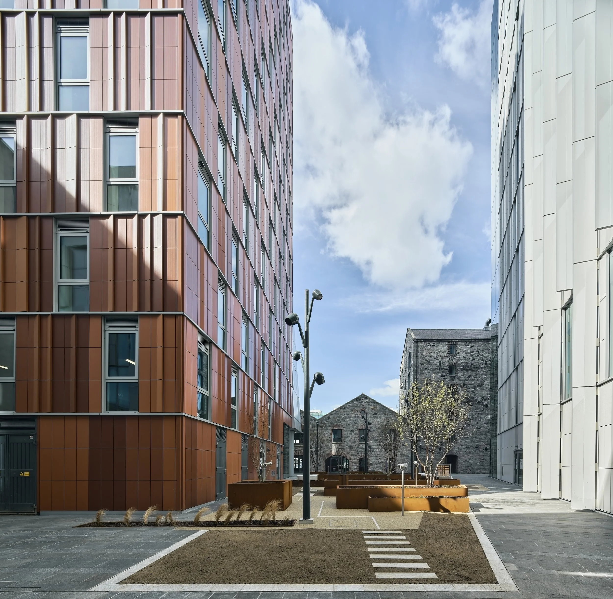Modern urban courtyard with colorful buildings, trees, benches, and a clear sky.