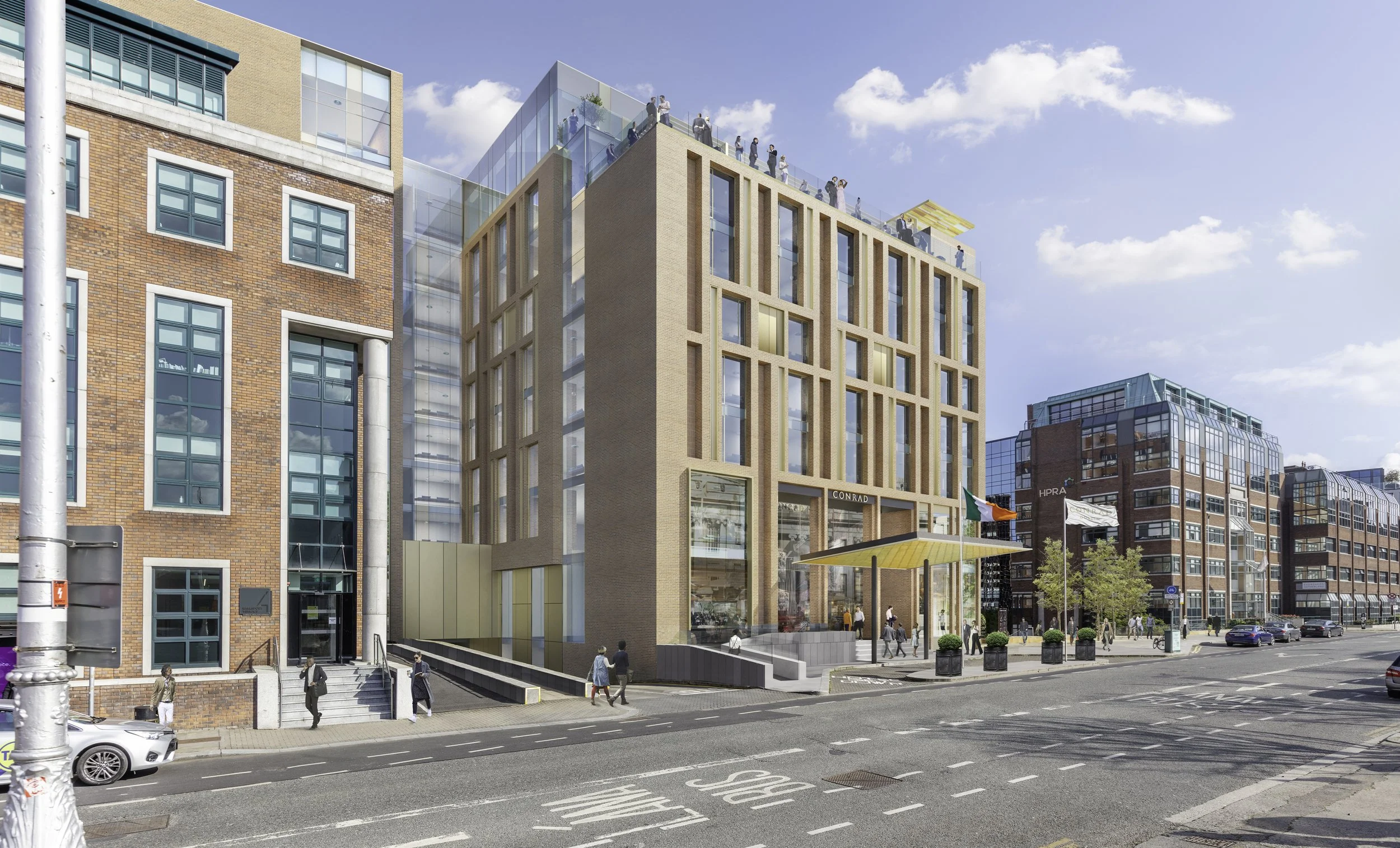 Modern mixed-use building with glass and brick facade, people walking on the sidewalk, flags, and a street with parked cars.