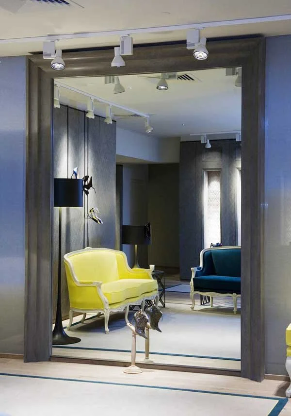 Modern living room with yellow and blue velvet sofas, wall-mounted lamps, and artistic sculptures.