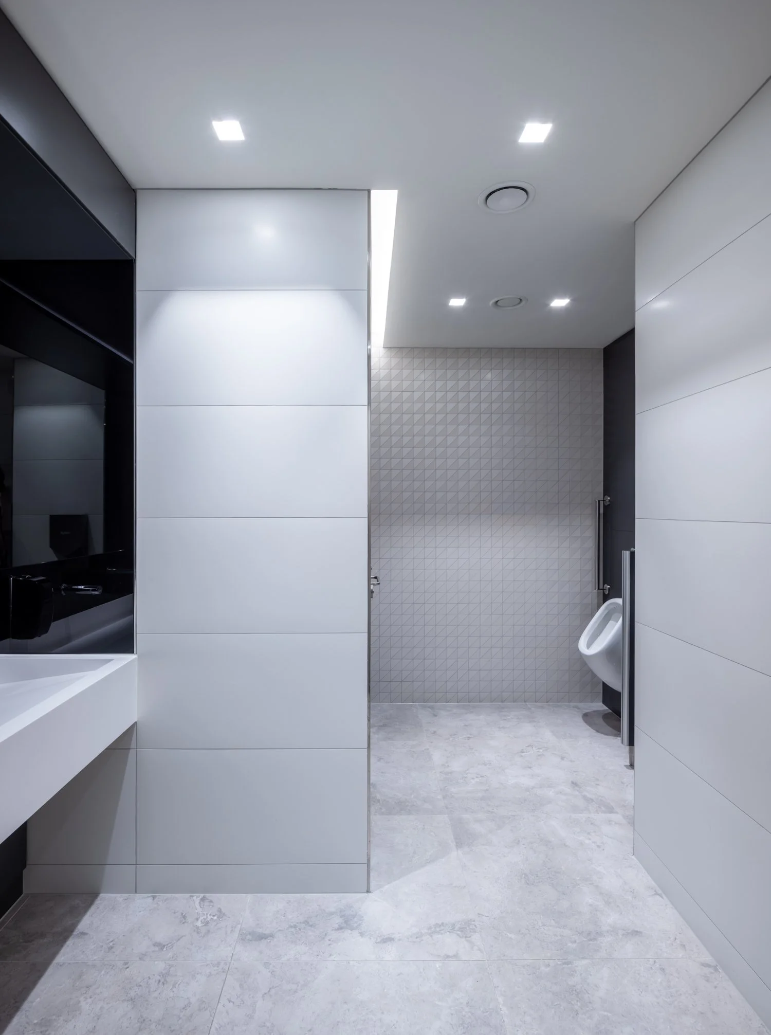 Modern men's restroom with urinal, gray tiled walls, white tiled walls, and gray tiled floor.