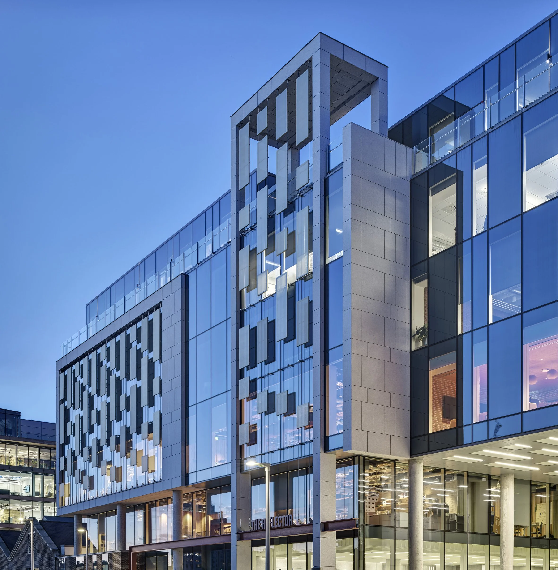 Modern office building with glass windows and decorative exterior panels, illuminated during twilight.