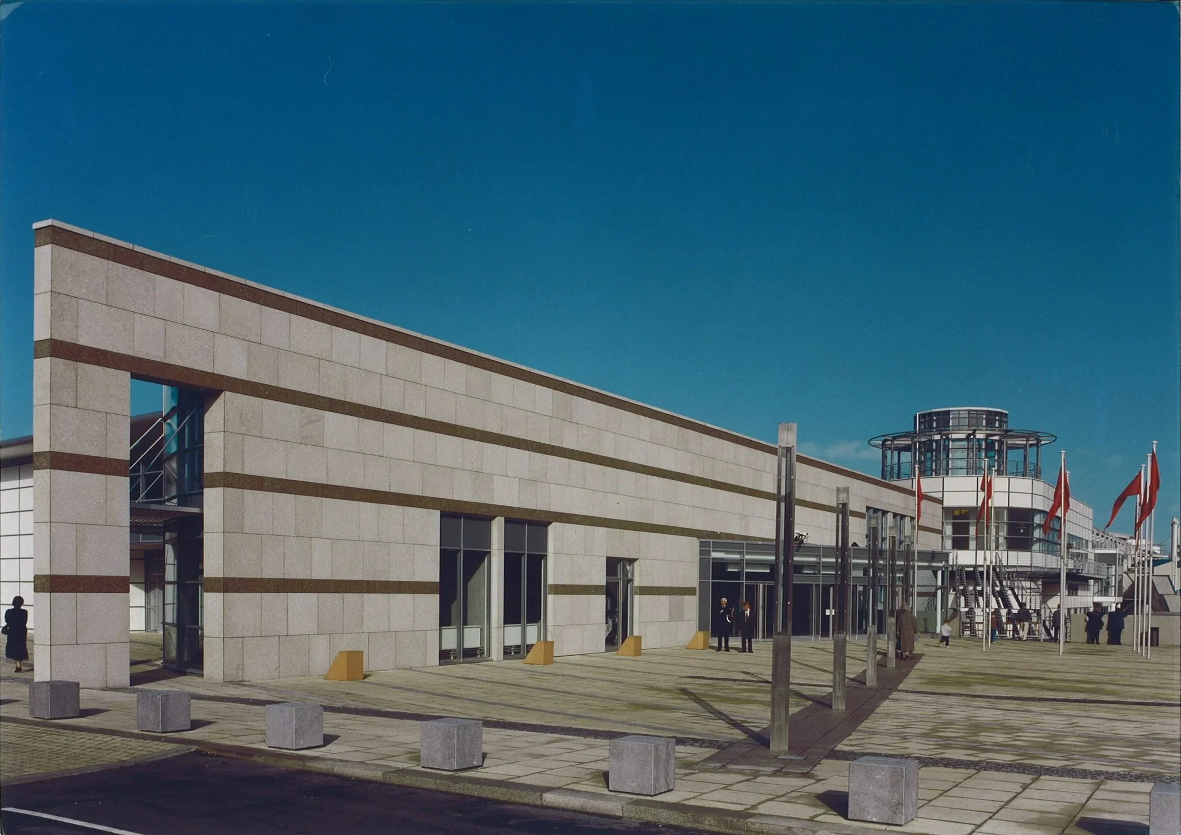 Modern building with flags, glass entrance, and clear blue sky.