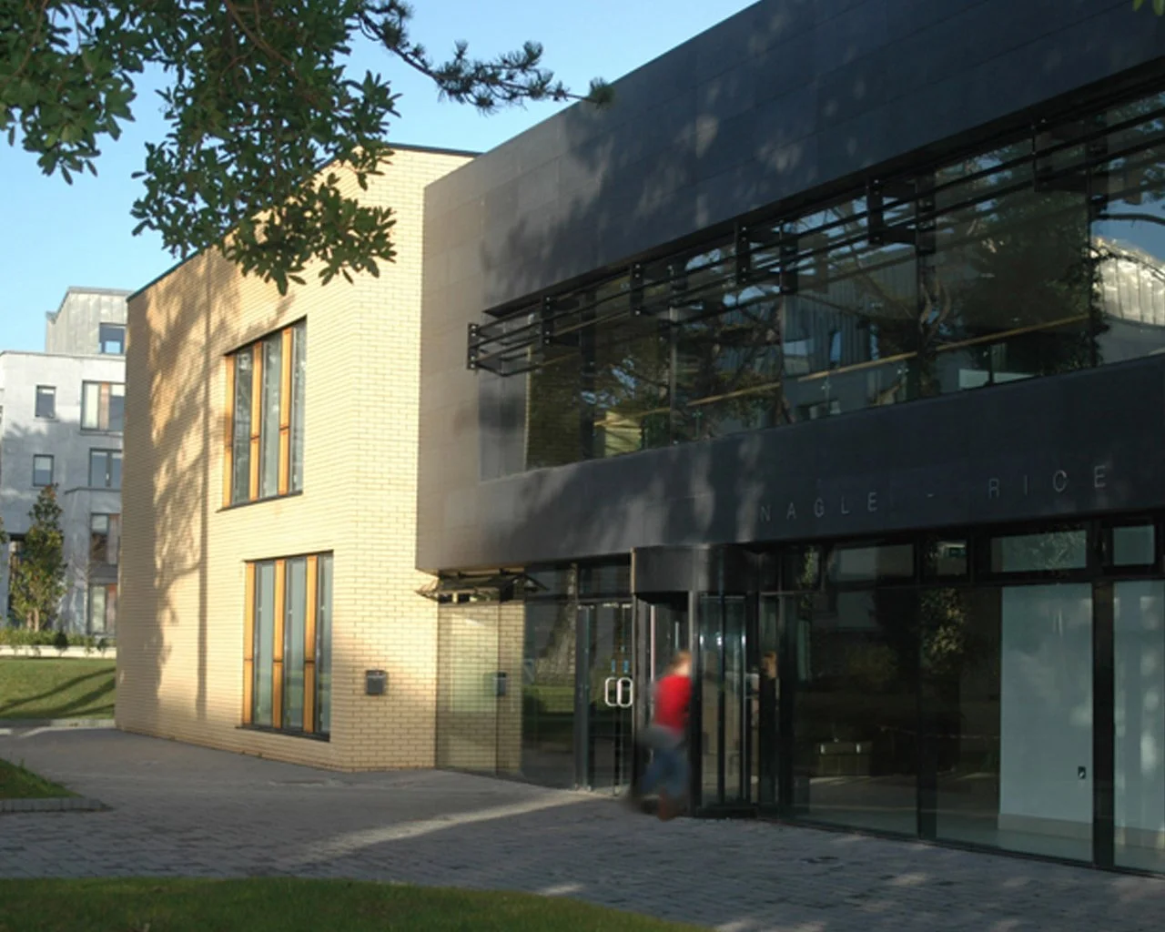 Modern building with brick and glass exterior, trees, and a person walking into the entrance.
