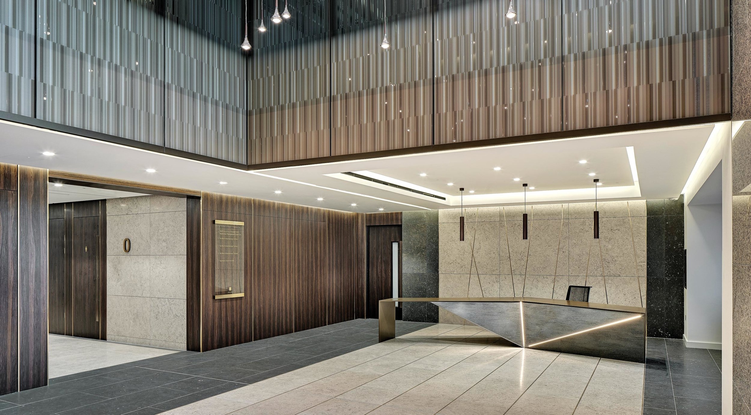 Modern office reception area with dark wood paneling, stone walls, a sleek angular reception desk with LED lighting, and pendant ceiling lights.
