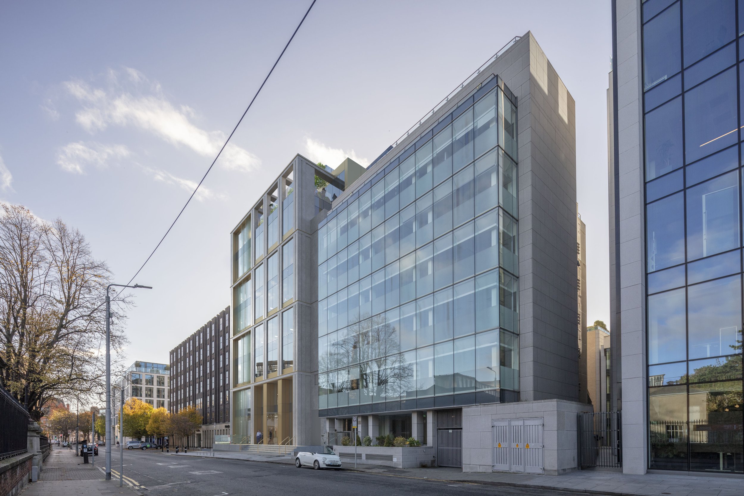 Street view of modern office buildings with glass facades and trees with autumn leaves.