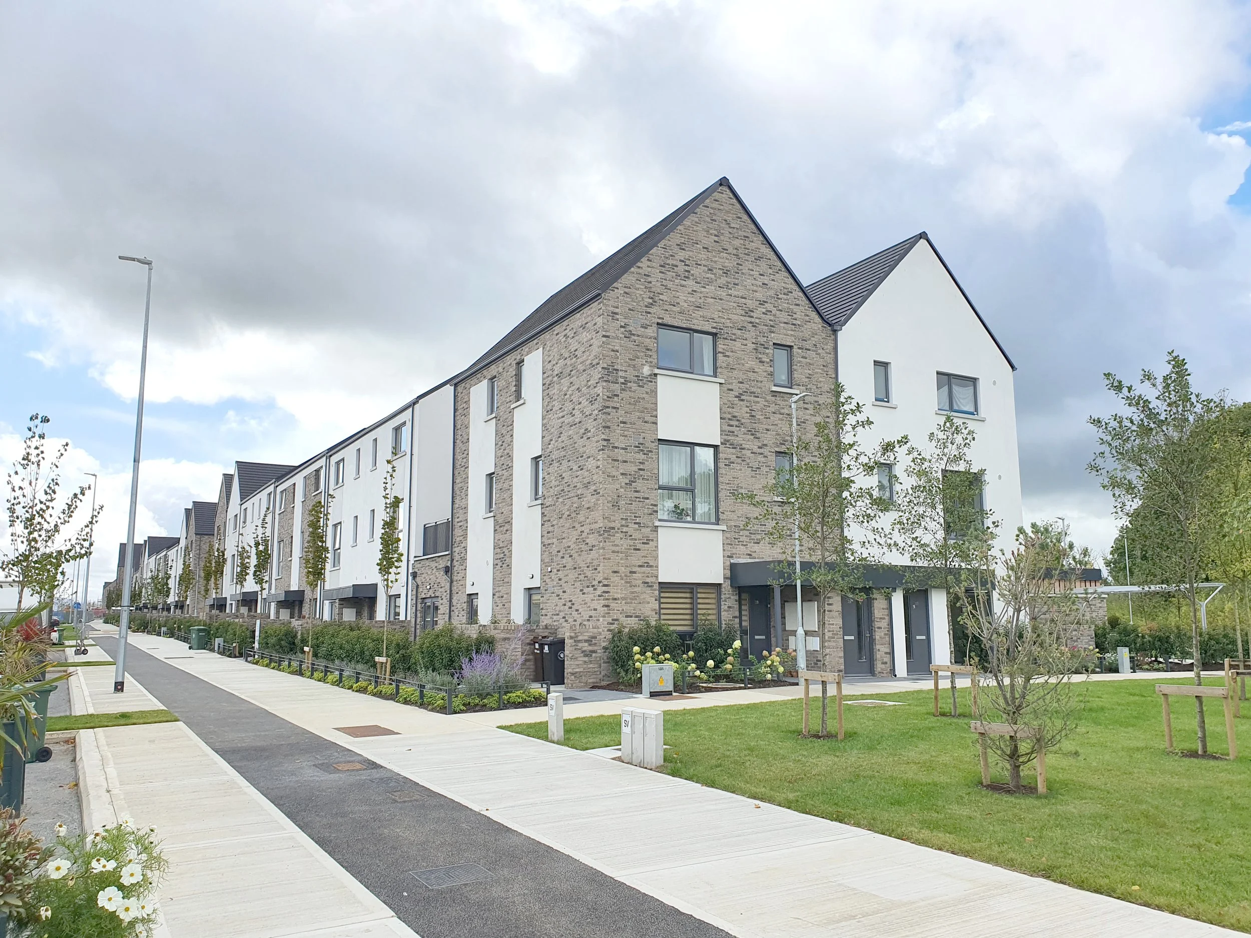 A modern residential street with new townhouses, young trees, and a paved sidewalk.