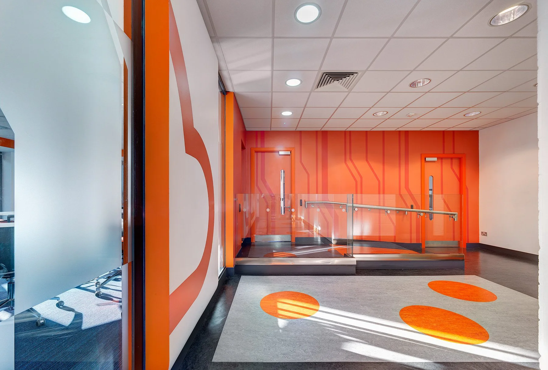 Interior of a modern building with orange walls, circuit pattern designs, and a glass door with a ramp for accessibility.