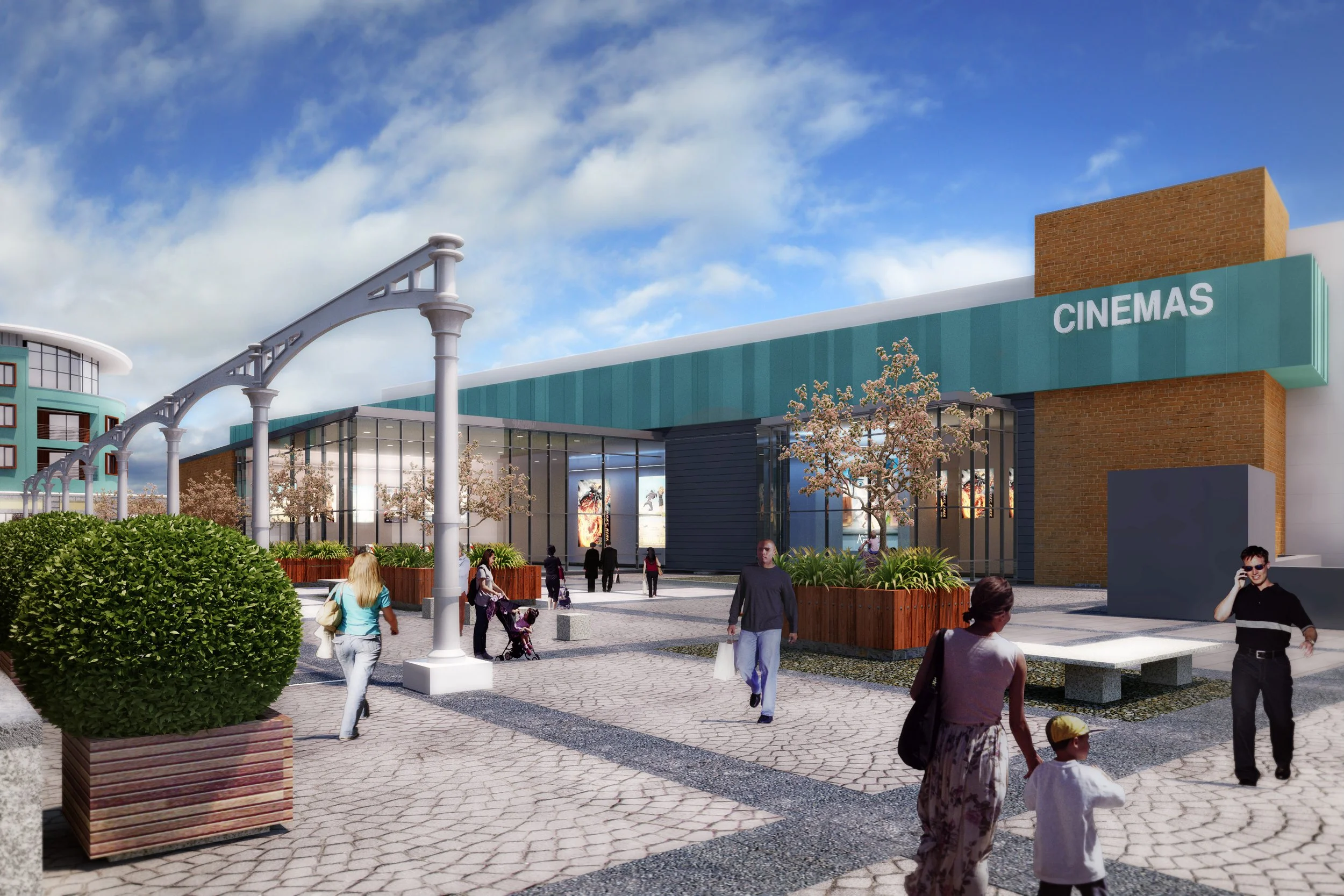 A modern outdoor shopping mall with a cinema and people walking on cobblestone paths, some talking on phones, others with children, surrounded by trees and planters, under a partly cloudy sky.