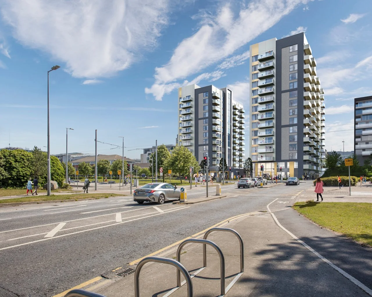 Street view with cars, pedestrians, and tall residential buildings on a sunny day with blue sky and clouds.
