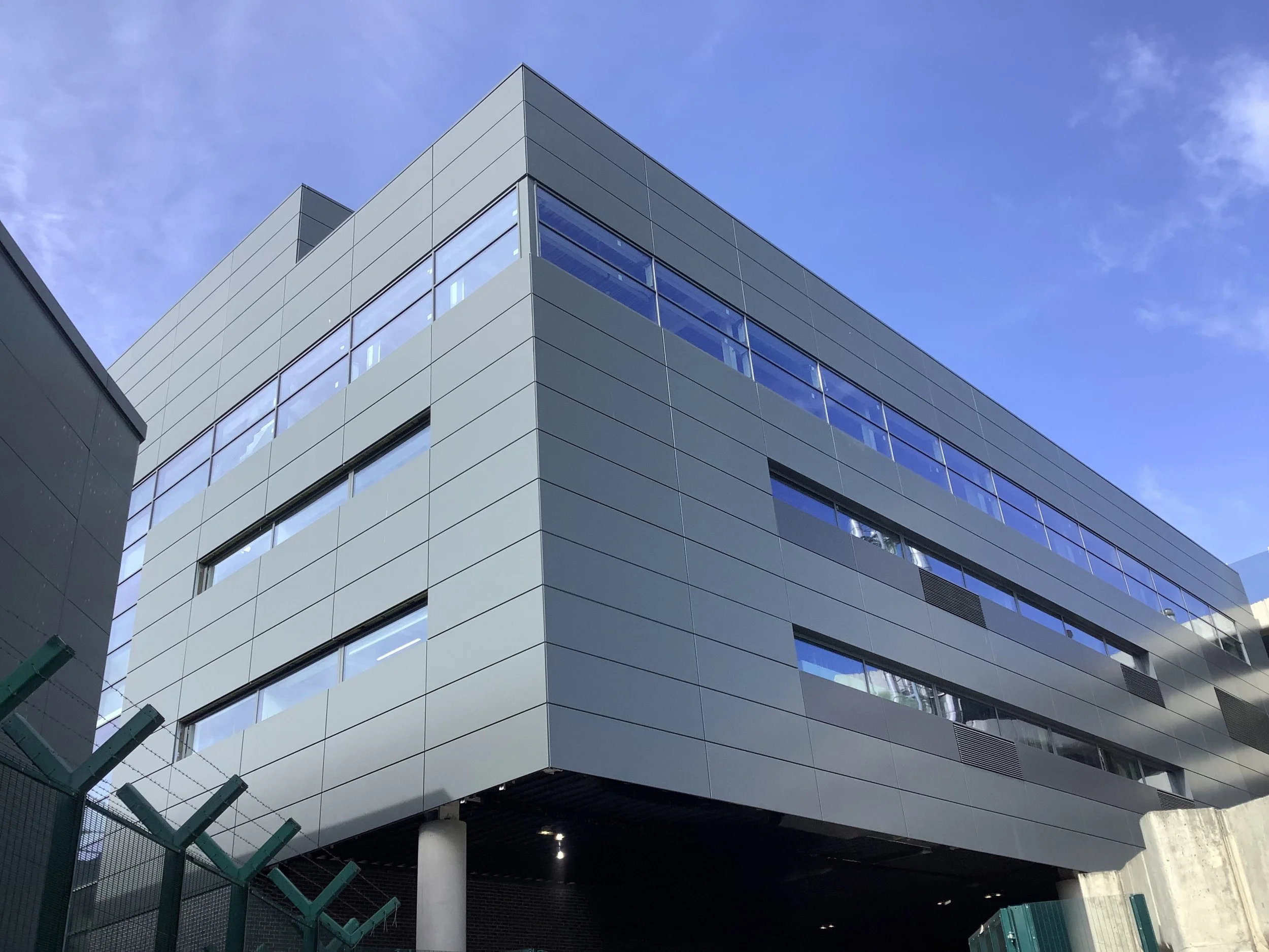 Modern gray building with large windows, black accents, and a clear blue sky.