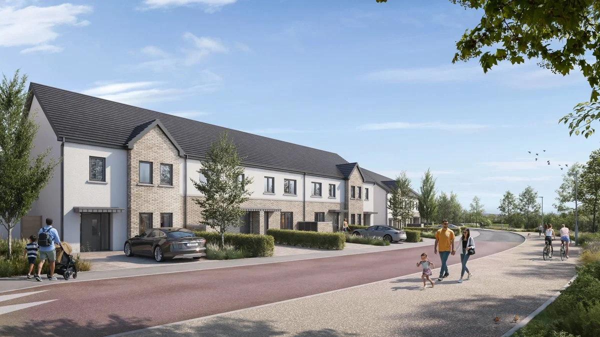 A suburban street with modern townhouses, parked cars, and people walking and biking on the sidewalk under a partly cloudy sky.