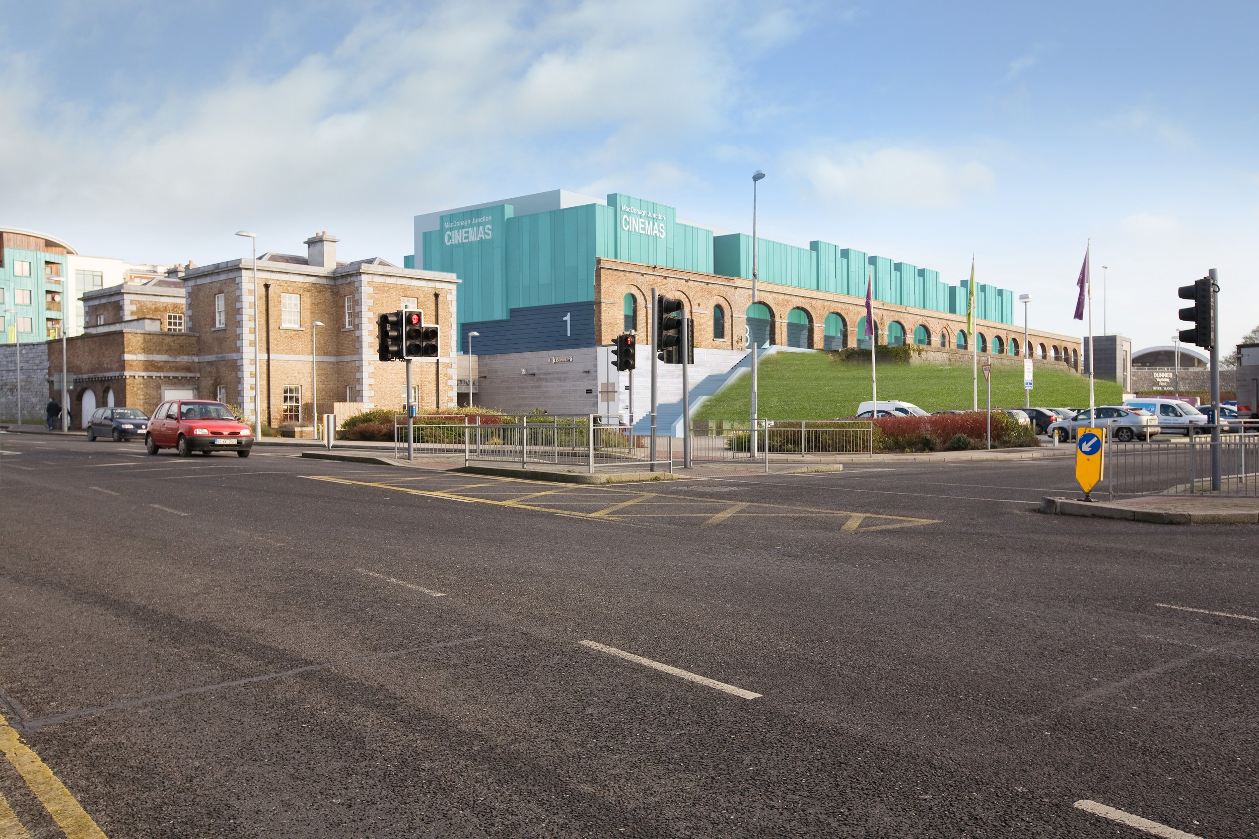 A city street intersection with traffic lights, cars, and a modern building with a sign that reads 'MacDonald Junction Cinemas' in the background.