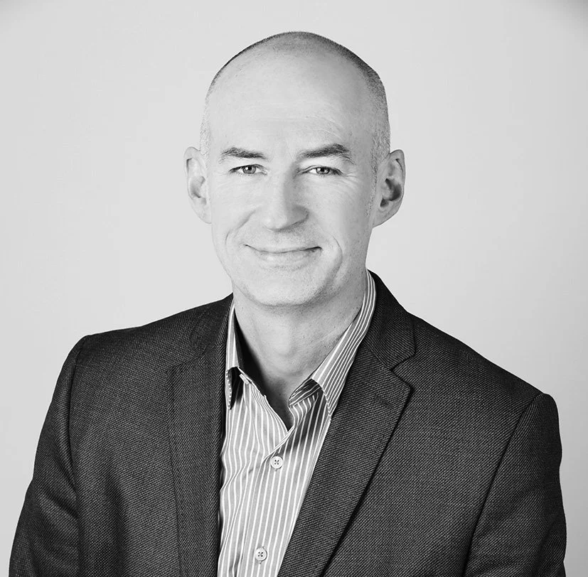 Black-and-white professional headshot of a smiling man wearing a suit and striped shirt.