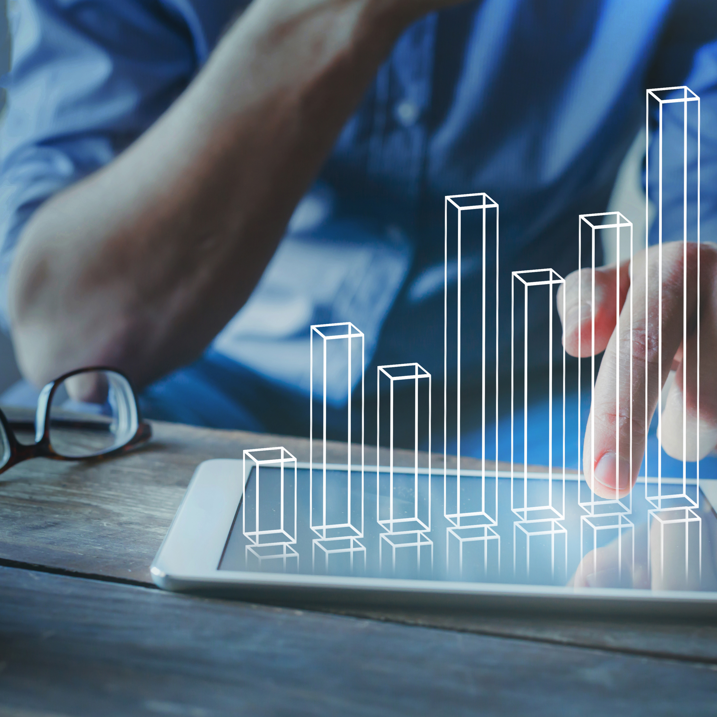 Person interacting with digital bar graph on tablet, wearing blue shirt, glasses nearby.