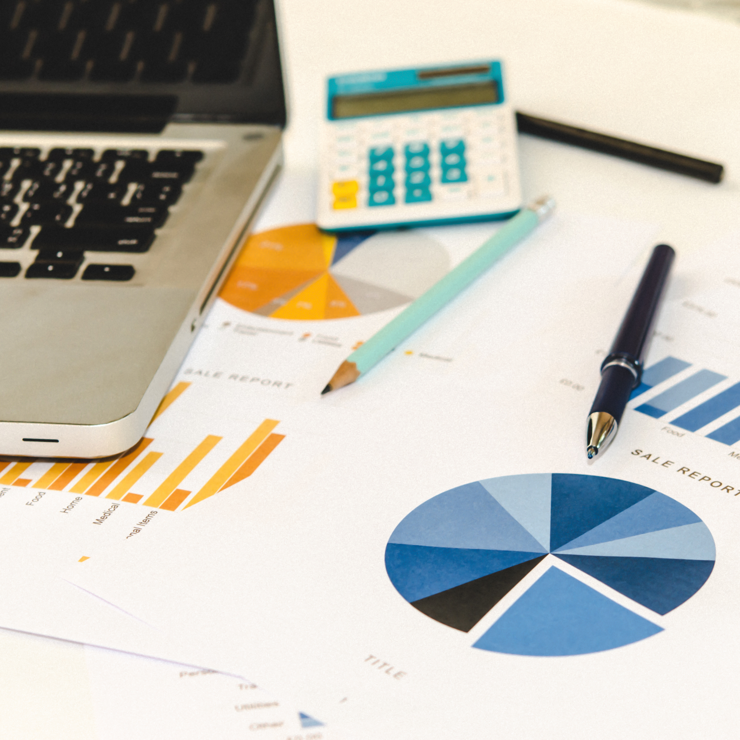 Laptop, calculator, pen, pencil, and sales report documents with charts on a desk.