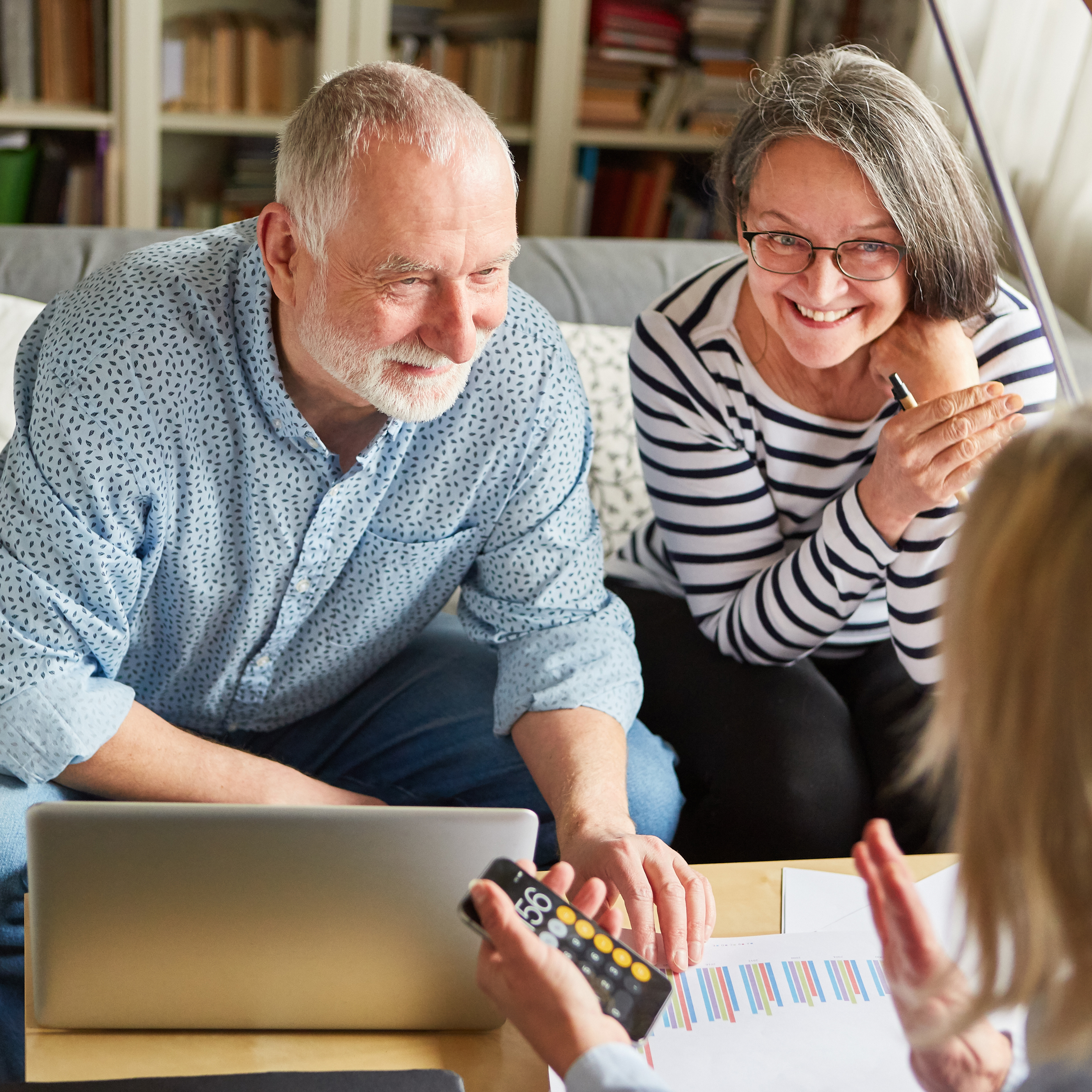 Smiling senior couple discussing financial documents with advisor at home, laptop and charts on table.