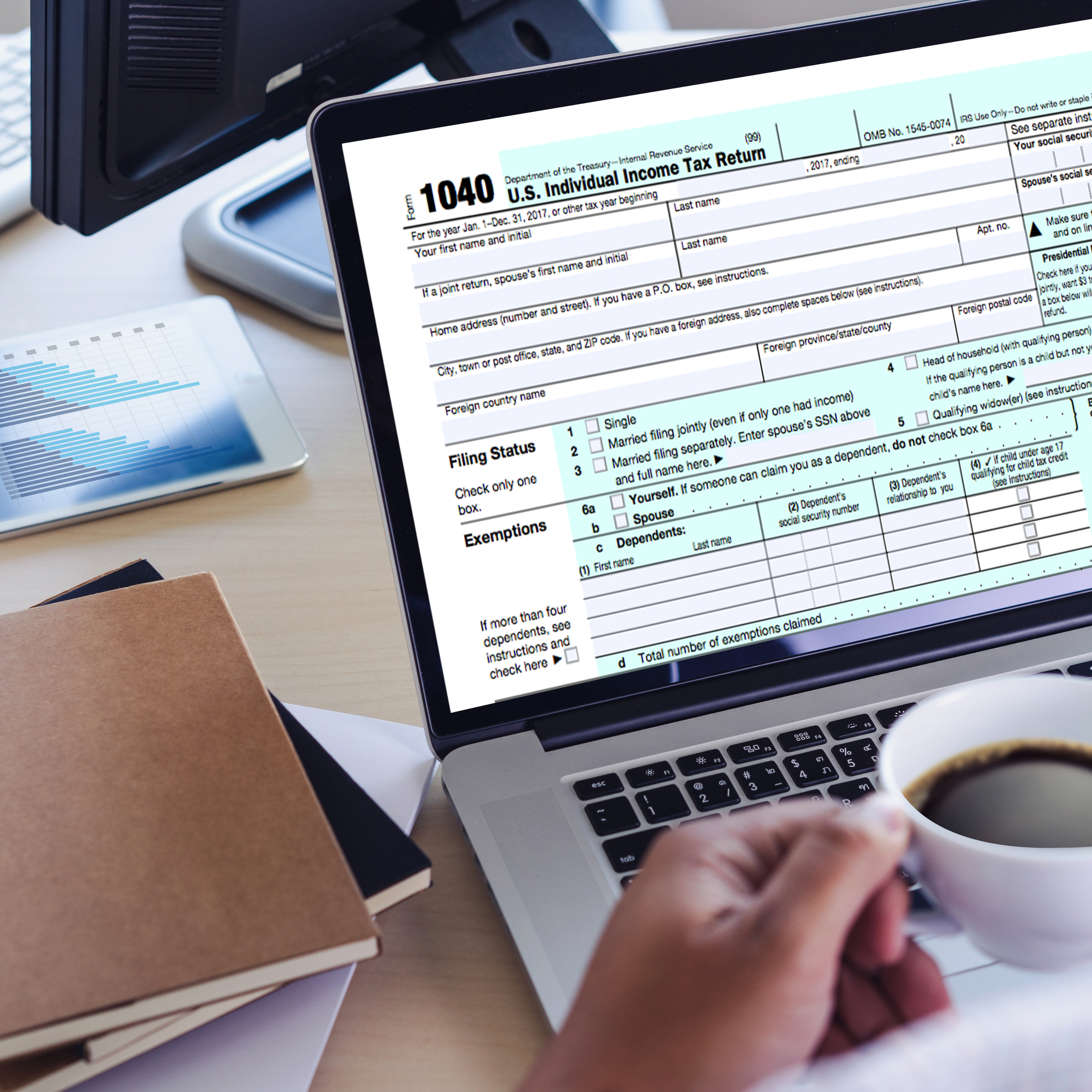 Person holding a coffee cup while viewing a Form 1040 U.S. Individual Income Tax Return on a laptop screen, with notebooks and a financial report on a desk.