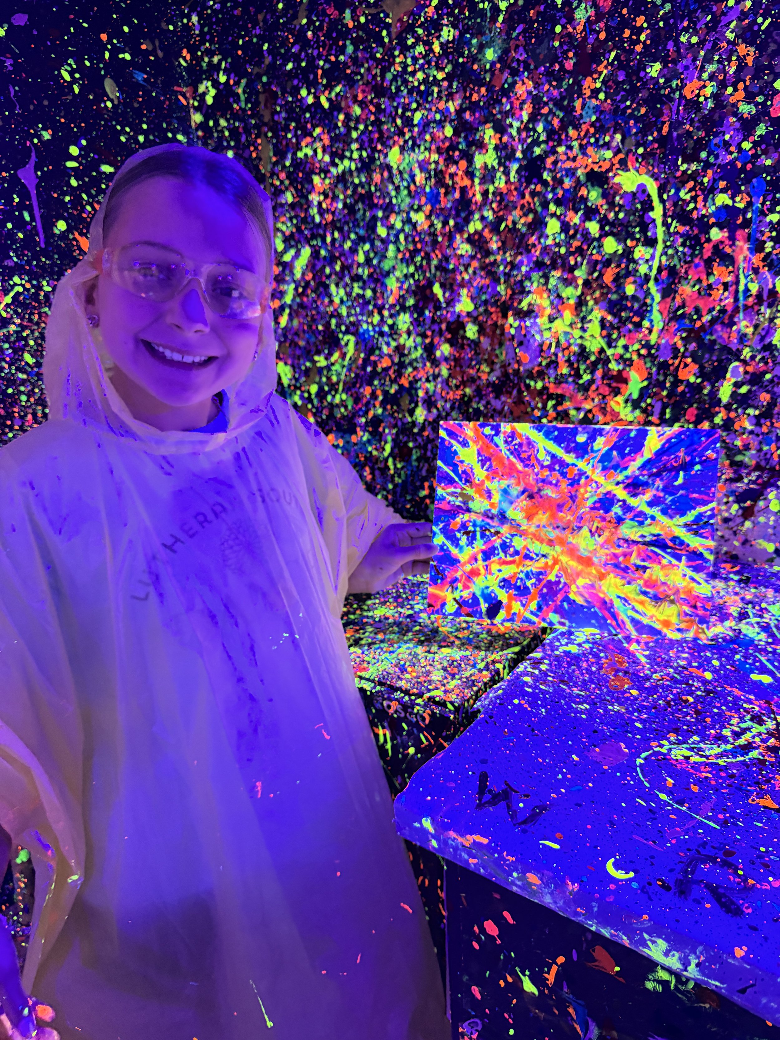 Girl in splattered room with a brightly colored abstract splatter painting.